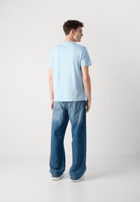 Světle modré bavlněné tričko s kulatým výstřihem, v kombinaci s volnými, vybledlými modrými džíny. Model zobrazen zezadu.