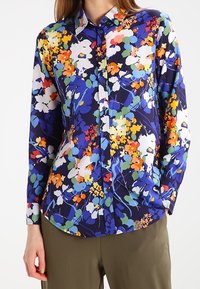 Skjorta med långa ärmar som har ett flerfärgat blommönster på en marinblå bakgrund, med knäppning framtill och strukturerad krage.