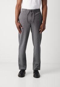 Pantaloni de trening gri cu talie reglabilă, având o textură moale, picioare drepte și buzunare laterale. Purtați cu pantofi negri.