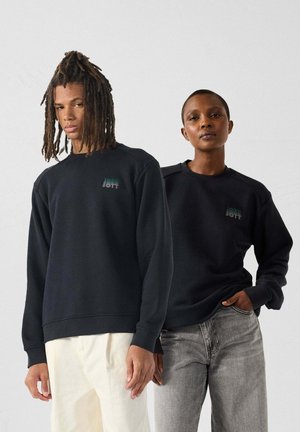 Sudaderas negras con puños y dobladillos acanalados. Una presenta un pequeño logo, ambas tienen un ajuste holgado y están hechas de una tela suave.
