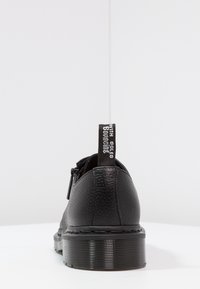 Chaussure en cuir noir avec surface texturée, bout arrondi et semelle épaisse à rayures. Comprend une languette avec le texte "WITH SOLES BOUNCING".