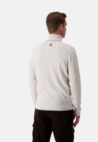 Hellbeige, gestrickter Pullover mit hohem Kragen und gerippten Bündchen. Verfügt über ein quadratisches braunes Etikett auf der Rückseite. Angenehme Textur, taillierte Passform.