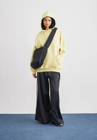 Rumena jopa s kapuco, črna torba poševno čez telo, kombinirana s črnimi hlačami širokih nogav. Gladek material in sproščen kroj.