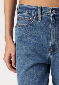 Jeans din denim albastru, cu un fit clasic, elemente din cupru, cusături vizibile și o ușoară textură în material. Talie standard.