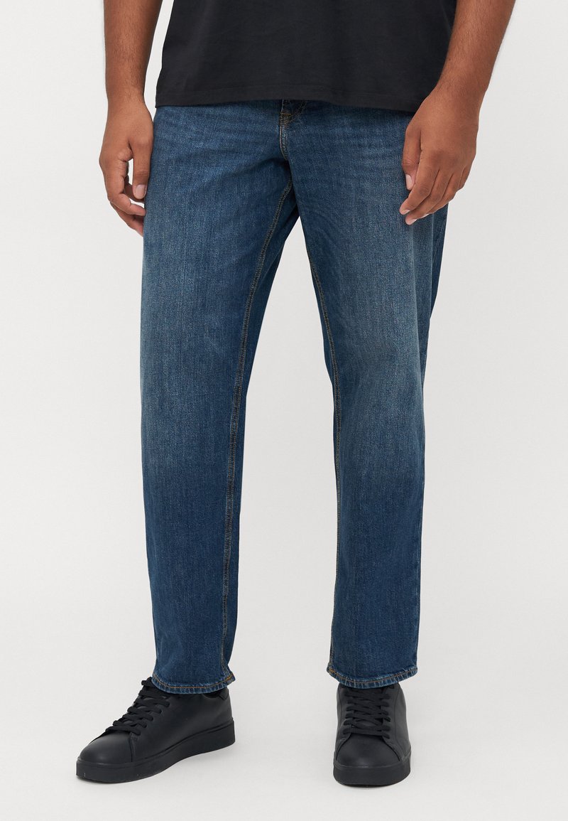 Blue denim jeans with a straight-leg cut, featuring stitched seams and a durable fabric texture. Worn with black sneakers.