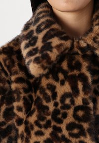 Manteau en fausse fourrure imprimé léopard avec un large col, présentant une texture douce et des nuances de marron et de noir dans des motifs variés.