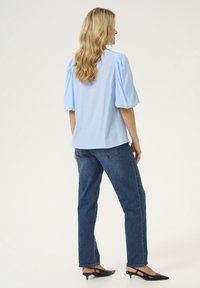 Gaiši zila puff-sleeve blūze, apvienota ar tumši zilām džinsiem. Blūzei ir gluda tekstūra, bet džinsiem ir klasiskā griezuma forma. Melni zamšādas kurpes ar papēžiem.