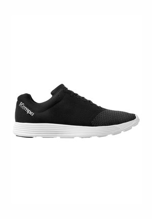 Chaussure de sport noire avec tige en tricot respirant, semelle en caoutchouc blanche et accents texturés. Présente un bout arrondi et un système de laçage. Marque "Kempa" affichée.