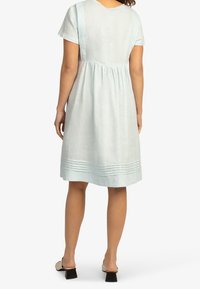 Jasnoniebieska sukienka z lnu, z krótkimi rękawami, marszczona w talii, z poziomym przeszyciem na dole. Tkanina ma teksturowane wykończenie.