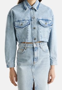 Avkortad ljusblå denimjacka med två bröstfickor, silverknappar och fransade kanter, i kombination med en matchande högmidjad denimkjol.