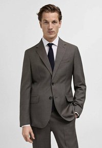 Gray tailored suit with a two-button closure, notch lapels, and side pockets. Paired with a white shirt and dark tie, displaying a sleek design.