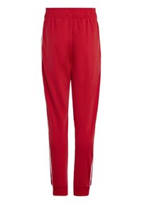 Rdeče atletske hlače z elastičnim pasom, zasnovo zoženih nogavic in belimi stranskimi črtami; gladka tkanina s rahlo sijočo teksturo.