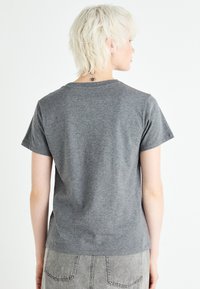 Camiseta gris de manga corta hecha de tela suave, con cuello redondo y un corte relajado, mostrada desde la vista trasera sobre un fondo blanco.