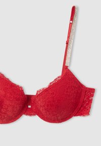 Reggiseno rosso in pizzo con coppe preformate, spalline in raso regolabili e un accentuato dettaglio di strass. Presenta un motivo floreale in pizzo e bordi ondulati.