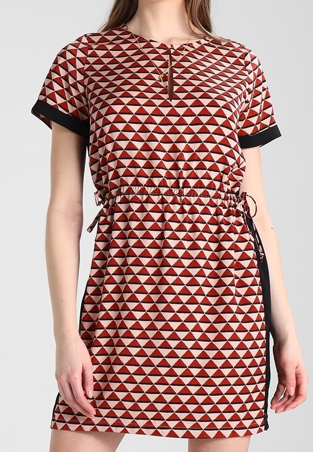 Femme portant une robe à manches courtes, au-dessus du genou, avec un motif de triangles rouges et noirs, des poignets de manches noirs et un cordon de serrage ajustable à la taille.