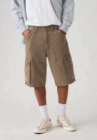 Cargo shorts in a light brown color, featuring two side pockets, made from durable fabric with a relaxed fit and stitched hem.