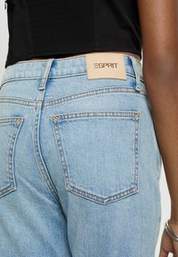 Jean en denim bleu clair avec une coupe ajustée, doté de deux poches arrière et d'une étiquette en cuir marron avec le logo "ESPRIT" embossé.