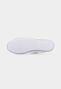 Πάτος ενός λευκού αθλητικού παπουτσιού φαίνεται από κάτω, με υφασμένο μοτίβο λαβής και στρογγυλεμένα δάχτυλα και τακούνι.