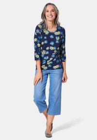 Dunkelbluse mit floralem Druck und Dreiviertelärmeln, kombiniert mit hellblauen, knöchellangen Jeans und grauen Ballerinas. Glattes Material und lockere Passform.