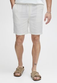 Hvide linnedshorts med elastisk talje, snor og subtil tekstur. Båret med brune ruskindsandaler med et enkelt stropdesign.