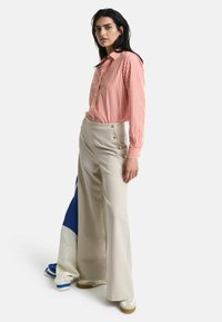 Camicia a righe rossa e bianca, abbinata a pantaloni larghi beige con dettagli in bottone dorato e sneakers chiare.