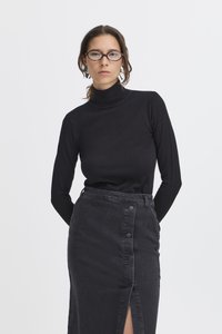 Haut noir à col roulé à manches longues associé à une jupe en denim noire taille haute avec une fente à l'avant et des boutons décoratifs.