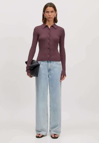 Koraalskleurig shirt met lange mouwen en ribbelstructuur, met een kraag en knoopsluiting, gecombineerd met lichtblauwe wijde jeans en een zwarte clutch.