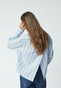 Hellblau gestreiftes Hemd mit gelben Linien, mit einem lockeren Schnitt und offenem Rückendesign, kombiniert mit blauen Jeans.