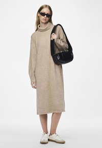 Robe en tricot beige avec col roulé et manches longues, finitions côtelées aux poignets et à l'ourlet ; associée à un sac à épaule noir et des baskets blanches. Design minimaliste.