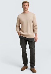 Beež kudumiga kampsun soonikkoes varrukaotste ja alläärega, kombineeritud tumeda halli teksapükste ja pruunide saapastega. Lihtne disain ja lõdvestunud lõige.