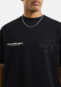 Camiseta de algodón negra con cuello redondo, mangas cortas, logo de texto blanco en el frente y un gráfico sutil en gris en el pecho.