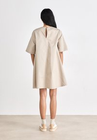 Vestido de algodão bege com mangas curtas e abertura em forma de chave nas costas. Combinado com tênis brancos com sola em tom neutro e meias claras.