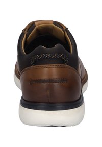 Bruine leren sneaker met een zwarte textielen kraag, witte rubberen zool en contrasterende stiksels. Afgeronde hak met minimale detailing.