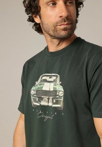 Camiseta de algodón verde oscuro con un gráfico de un coche antiguo con rayas blancas, cuello redondo y mangas cortas.