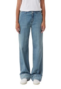 Niebieskie dżinsy o szerokich nogawkach z efektem sprania, wyposażone w standardowy pas, pięć kieszeni i podwinięte nogawki, zestawione z białymi trampkami.