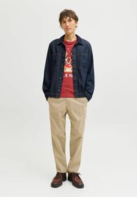 Mørkeblå denimjakke med lange ærmer og knapper foran; rød t-shirt med grafik; beige bukser; brune sko med sorte såler.
