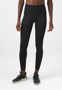 Fekete, magas derekú leggings, struktúrált panelekkel és varrási részletekkel, fekete és szürke sportcipőkkel párosítva.