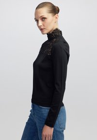 Zwarte langemouwen top met een hoge kanten kraag en gestructureerde lijf, gecombineerd met blauwe denim. Heeft een getailleerd silhouet en een eenvoudig ontwerp.