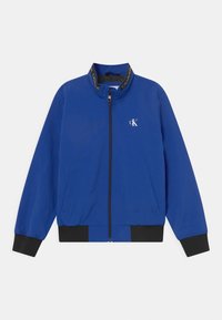 Niebieska bombka z zamkiem z przodu, elastycznymi mankietami i dołem. Posiada czarny pasek wokół kołnierza z logo "CALVIN KLEIN". Lekki materiał.