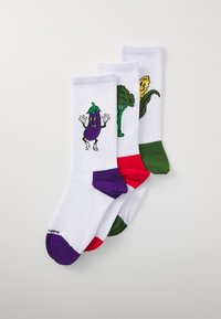 Trois paires de chaussettes blanches montantes avec des motifs de légumes colorés : aubergine violette, brocoli vert et maïs jaune. Texture côtelée.