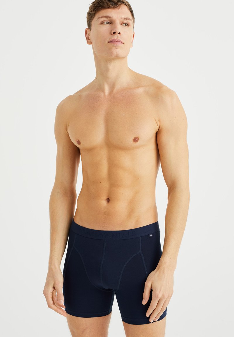 Boxers bleus marine avec une texture douce, un design ajusté et une large ceinture élastique affichant le mot "FONDAMENTAUX" dans un motif subtil.