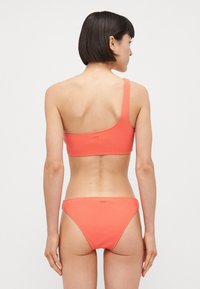 Top de bikini cu un umăr și fund special asortat în culoarea coral, având un material texturat și un detaliu subtil de branding. Material neted și elastic.