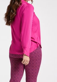 Fuchsia silk blouse with long sleeves, side slits, paired with patterned leggings featuring a geometric design in purple and pink hues.
