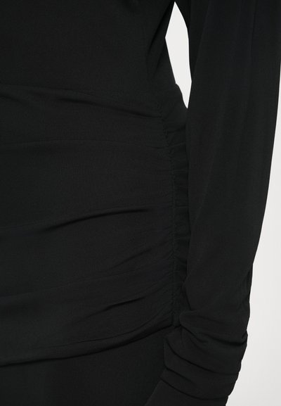 Fekete ruha, oldalán összegyűrt részletekkel és hosszú ujjakkal, sima, puha tapintású anyagból készült, karcsúsított sziluettért.