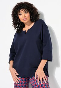 Top lungo a maniche lunghe blu navy con scollatura a V, caratterizzato da una vestibilità comoda e spacchi laterali. Tessuto morbido e liscio. Abbinato a pantaloni a fantasia.