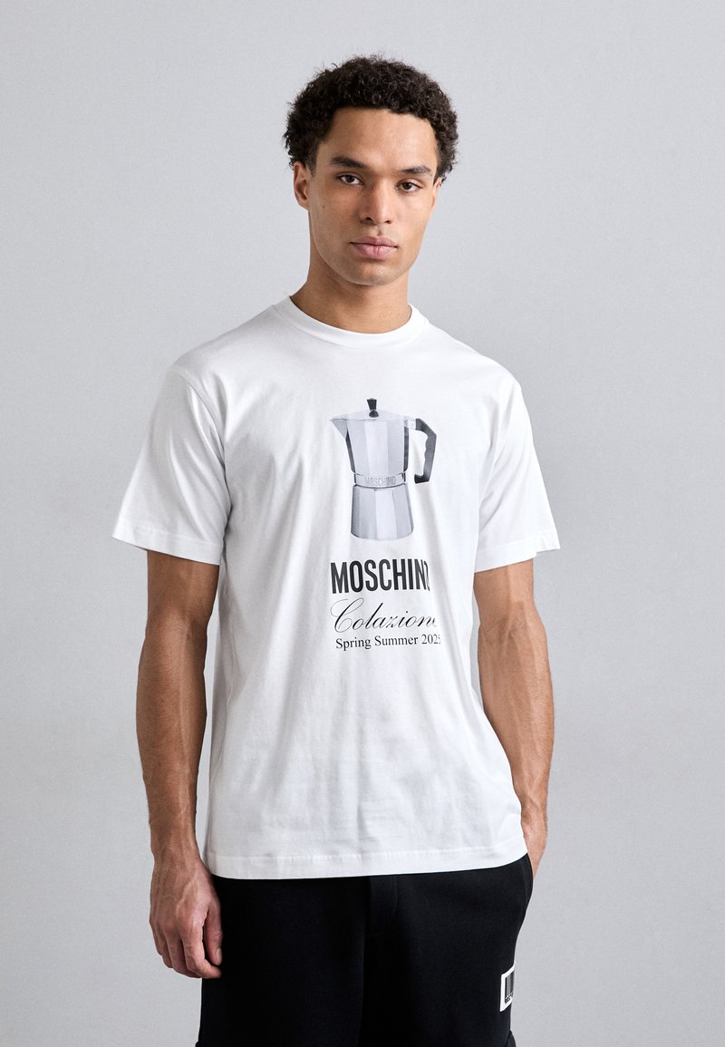 T-shirt en coton blanc avec un graphique d'une cafetière moka et le texte : "Moschino Colazione Printemps Été 2023" en police noire. Manches courtes.