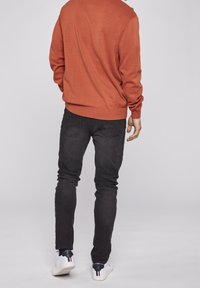 Orange stickad tröja, svarta slim-fit jeans och vita sneakers med färgade accenter. Tröjan har ribbade muddar och nederkant.