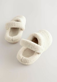 Zapatillas de felpa blancas y esponjosas con una forma redondeada, que cuentan con dos correas de tela anchas en la parte superior para un ajuste seguro. Textura suave.