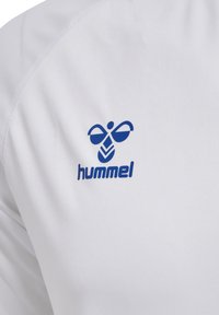 Witte sportshirt met een blauw Hummel-logo en een gestileerd bijen- en bladdesign op de linkerschouder. Glad stoftextuur.