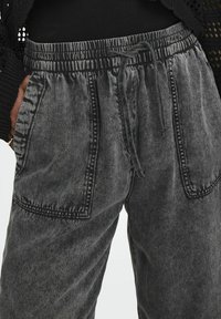 Grå denim-joggers med elastisk midjeband och dragsko, med två stora framskjutna fickor och kontrasterande sömnadsdetaljer.